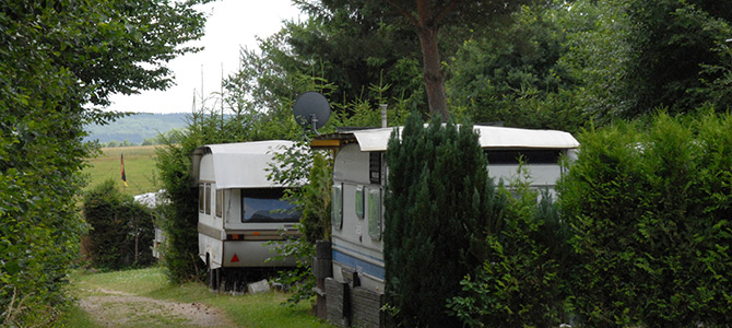Zwei Wohnwagen sind auf einer von dichtem Grün und Bäumen umgebenen Wiese geparkt, in deren Nähe eine Satellitenschüssel angebracht ist.