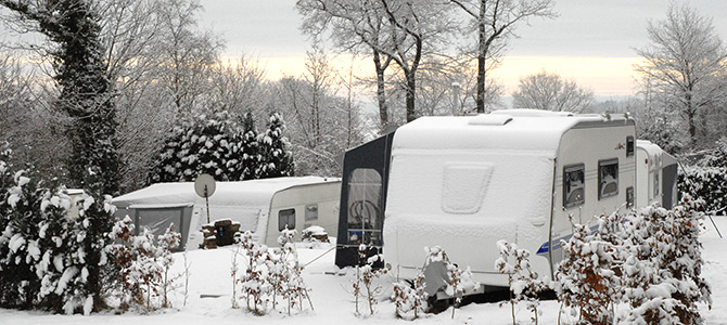 Mehrere Wohnwagen sind im Winter im Freien geparkt, mit Schnee bedeckt, mit Bäumen und Sträuchern im Hintergrund.