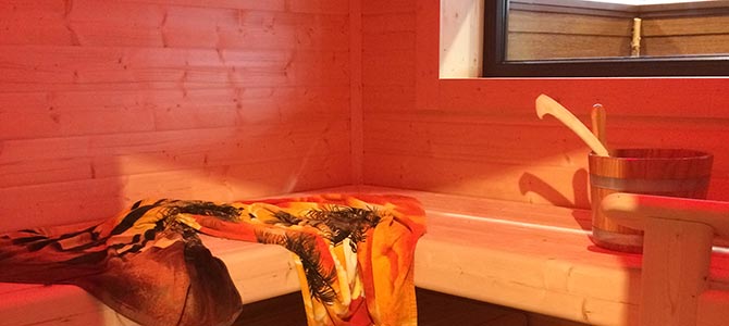 Sauna interior features warm wooden benches, a towel draped over one, and a classic wooden bucket with a ladle placed nearby under gentle lighting.