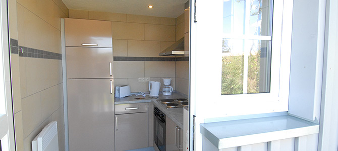 Small modern kitchen with beige cabinets, a refrigerator, a stove, a coffee maker, and a window view to the outside.