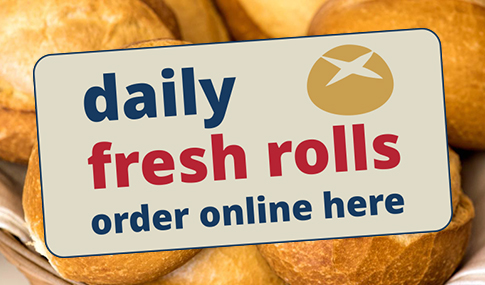 Ein Schild mit der Aufschrift Täglich frische Brötchen hier online bestellen steht vor einem Stapel Brötchen.