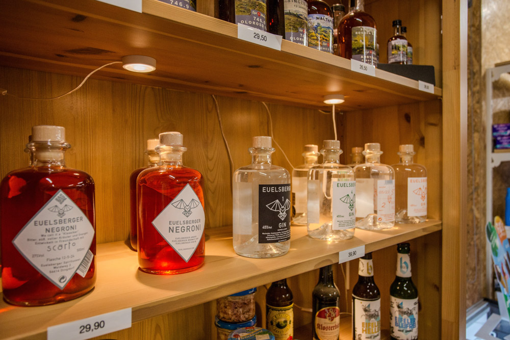 Die Flaschen mit Spirituosen und anderen alkoholischen Getränken stehen in Holzregalen, die jeweils mit Preisen beschriftet sind.