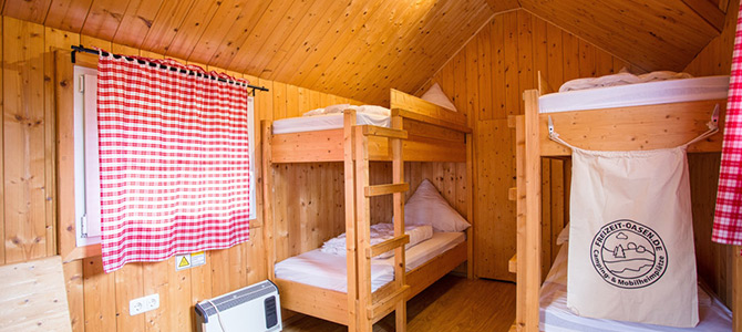 Holzgetäfeltes Zimmer mit zwei hölzernen Etagenbetten, weißem Bettzeug, einem Fenster mit rot karierten Vorhängen und einer kleinen Wandheizung.